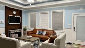 Un salon avec un canapé en cuir marron, des fauteuils beiges, une table basse en bois et un ventilateur de plafond.