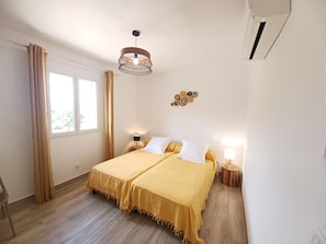 Ein Schlafzimmer mit Doppelbett, einem fenster mit Vorhängen, einer Pendelleuchte und einer Wand-Klimaanlage.