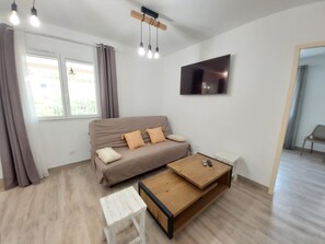 A modern living room with a sofa, a coffee table, a TV, and a window with curtains.