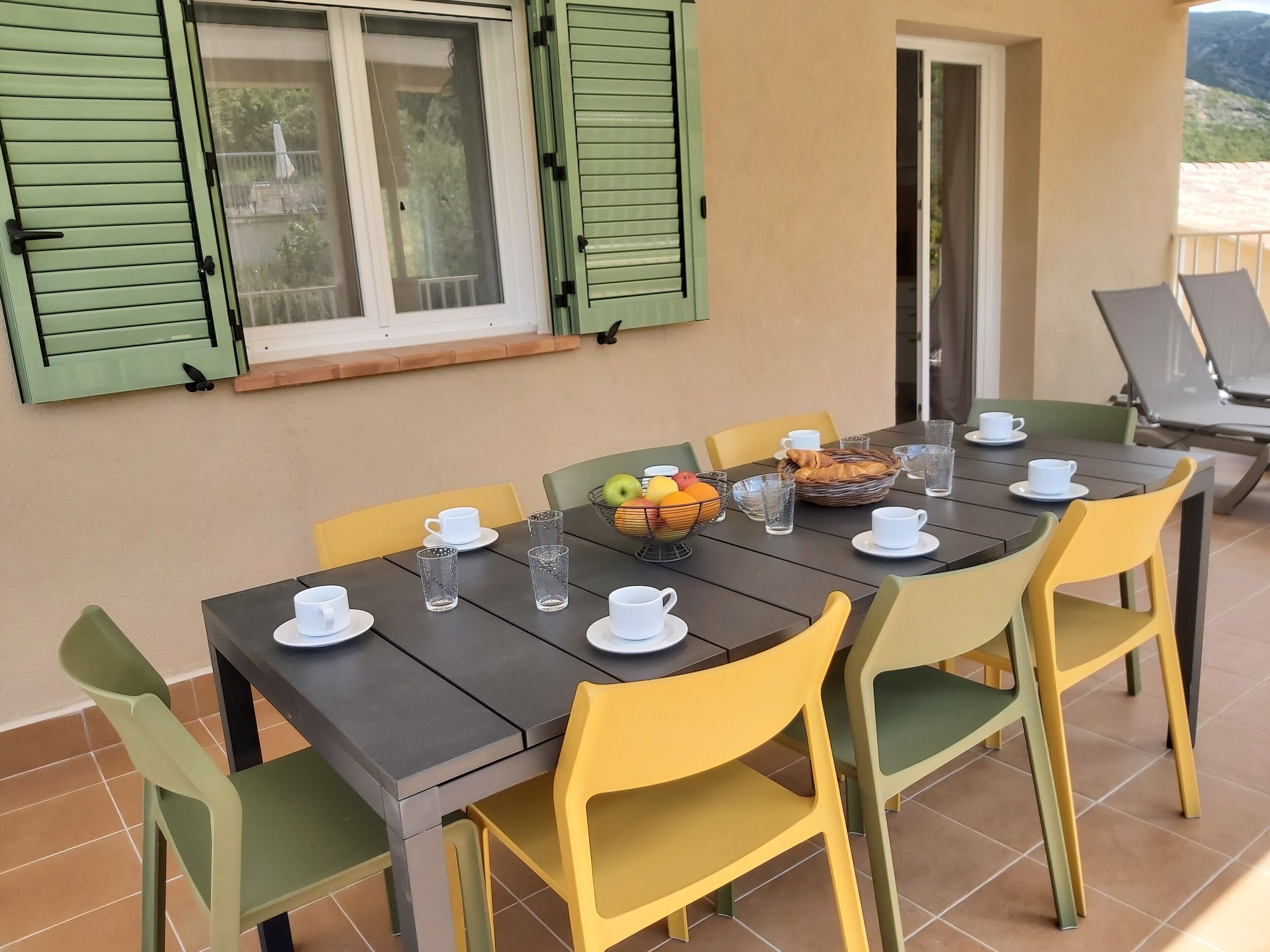 A dining area with a table set for four, chairs, a window with shutters, and a view of the outdoors.