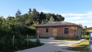 A wooden cabin with a gravel driveway, surrounded by greenery and trees. - Chalet Bois Piscine Individuelle Dordogne (Saint-Hilaire-d'Estissac)