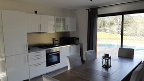A modern kitchen with white cabinets, a dining table with chairs, and a view of the outdoors through large windows. - Chalet Bois Piscine Individuelle Dordogne (Saint-Hilaire-d'Estissac)