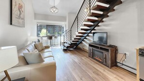 Un salon moderne avec un escalier en bois, un canapé, un téléviseur et une cheminée.