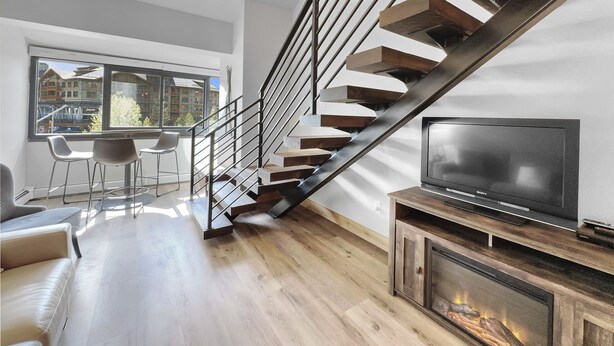 Un salon moderne avec un escalier en bois, une cheminée et un grand téléviseur.