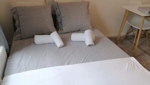 Ein ordentlich bezogenes Bett mit gestreifter Bettwäsche und Kissen, ein kleiner Tisch mit einem Stuhl und ein Holzboden.