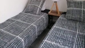 Ein Zimmer mit zwei Einzelbetten, jeweils mit einem schwarz-weiß karierten Bettüberwurf und passenden Kissen. Ein Nachttisch mit Lampe sowie zwei gerahmte Bilder an der Wand sind ebenfalls vorhanden.
