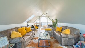 Un loft spacieux avec de hauts plafonds, des canapés en cuir avec des coussins jaunes, une table basse en verre et une vue sur la ville grâce à de grandes fenêtres.