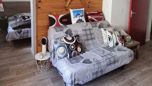 A bedroom with a wooden wall, a bed with patterned bedding, a bedside table, and a red door. - 4/6-person apartment in Saint-Sorlin-d'Arves at the foot of the slopes (Saint-Sorlin-d'Arves)