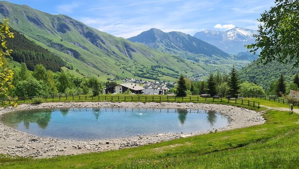 A serene pond surrounded by a wooden fence, with a small building in the background and mountains in the distance. - 4/6-person apartment in Saint-Sorlin-d'Arves at the foot of the slopes (Saint-Sorlin-d'Arves)