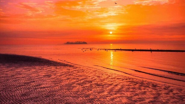 Ein Strand bei Sonnenuntergang mit klarem Himmel und ruhigem Wasser.