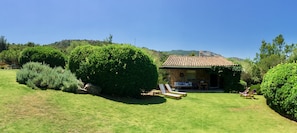 Casa de piedra con tejado de baldosas, rodeada de césped y setos bien cuidados. Hay dos sillones de exterior.
