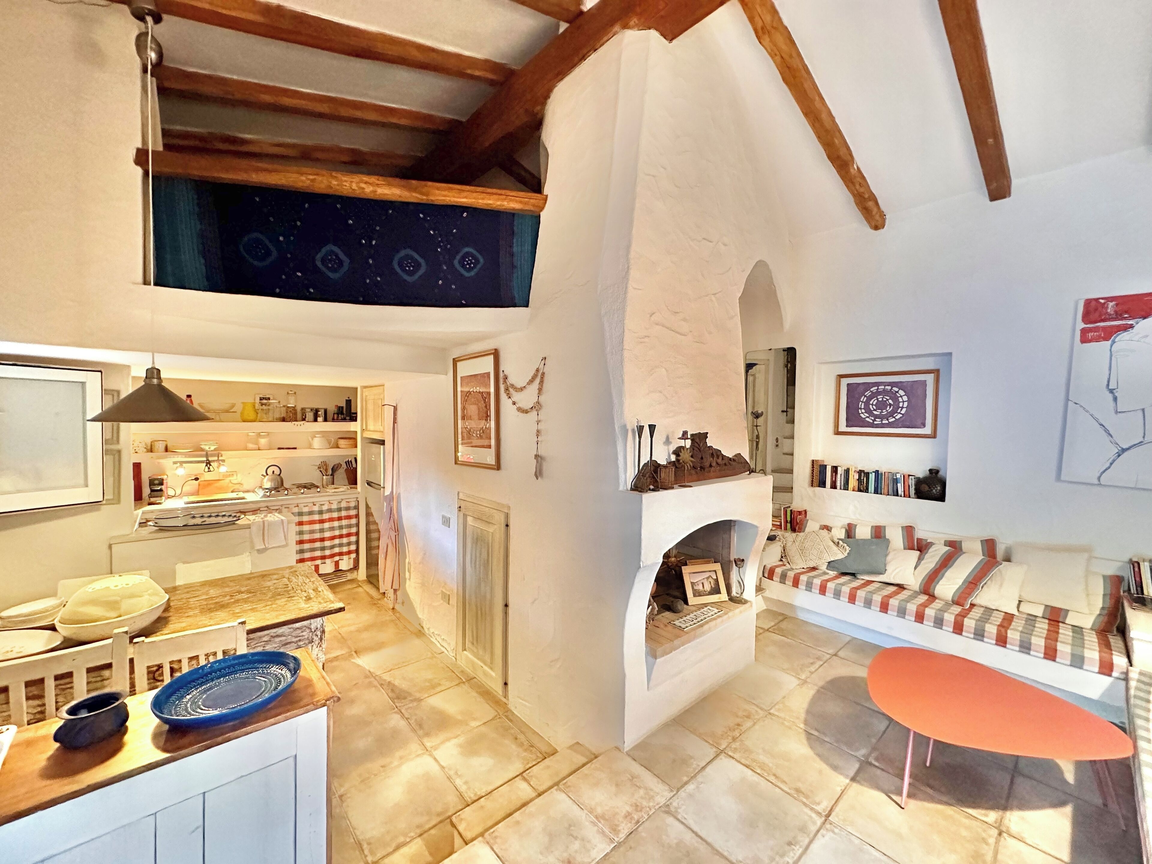 Una sala de estar acogedora con chimenea, un comedor con cocina al fondo y un altillo superior.