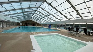 Una piscina interior con techo de vidrio, zona poco profunda separada y sillones de descanso.