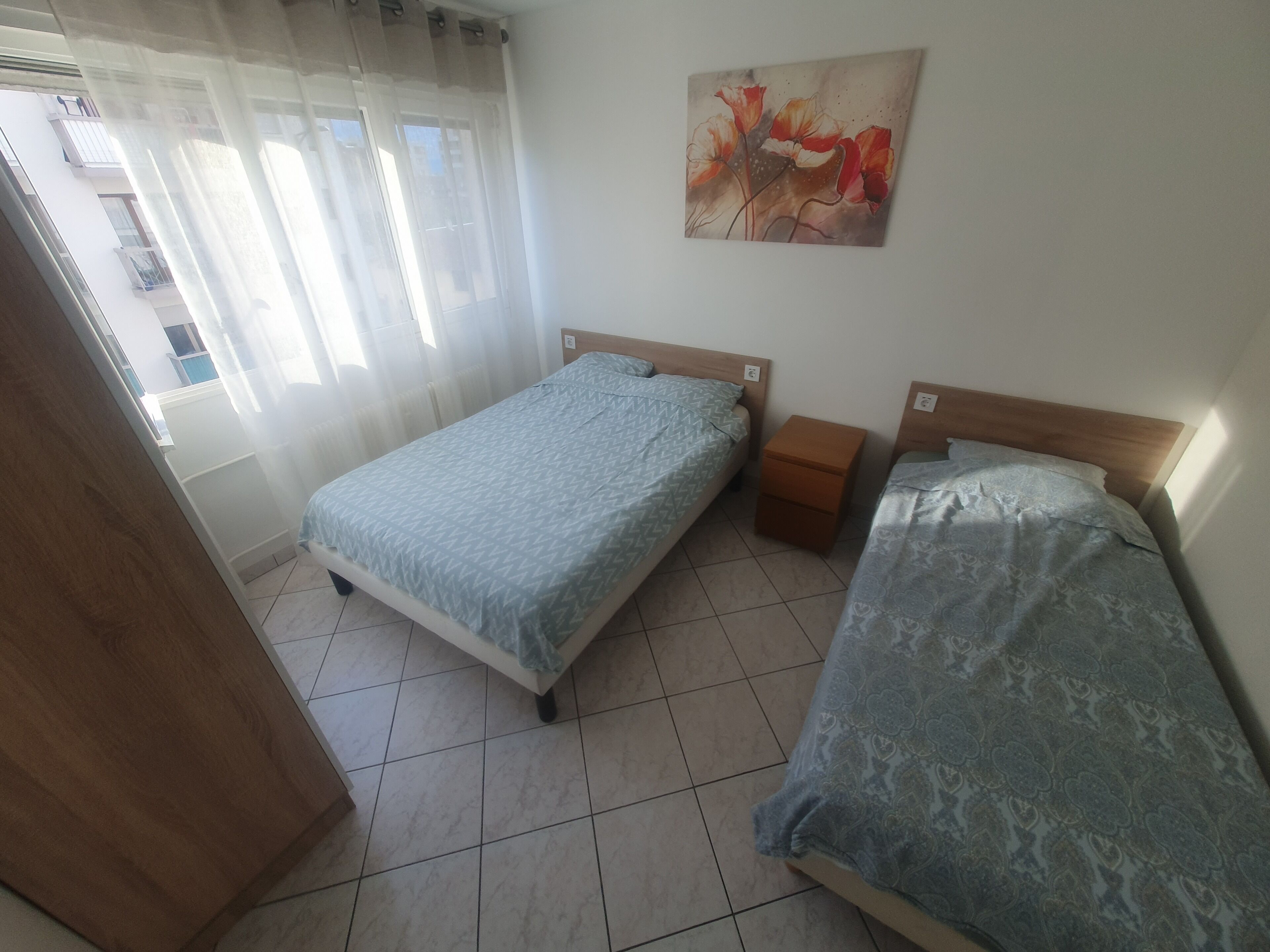 Un dormitorio con dos camas, una mesita de noche, un cuadro y una ventana con cortinas.