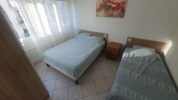 Un dormitorio con dos camas, una mesita de noche, un cuadro y una ventana con cortinas.