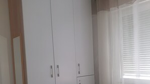 Un dormitorio con cama, armario, espejo y ventana con cortinas.