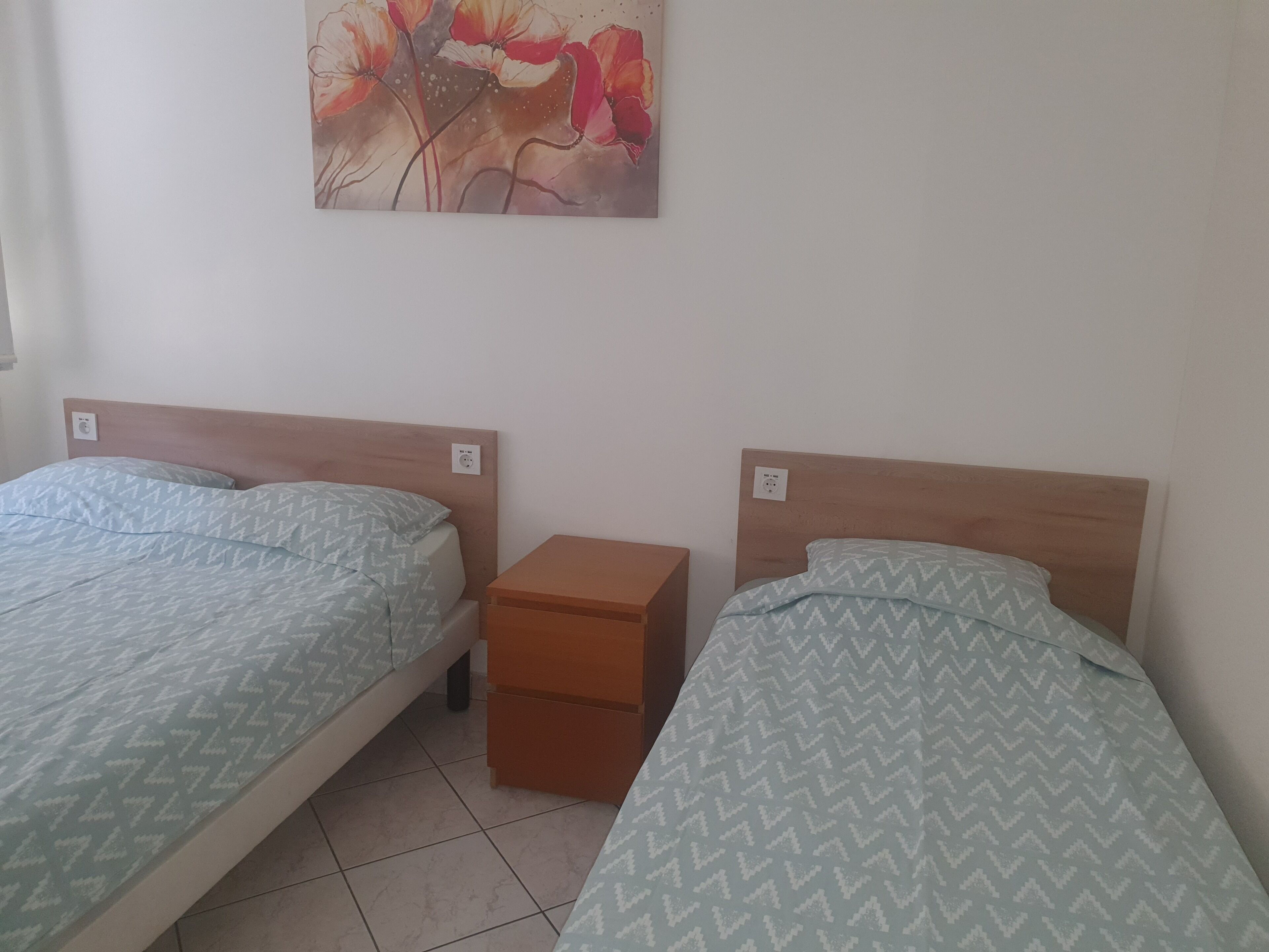 Two single beds with wooden headboards, a small wooden nightstand, and a wall-mounted power outlet.