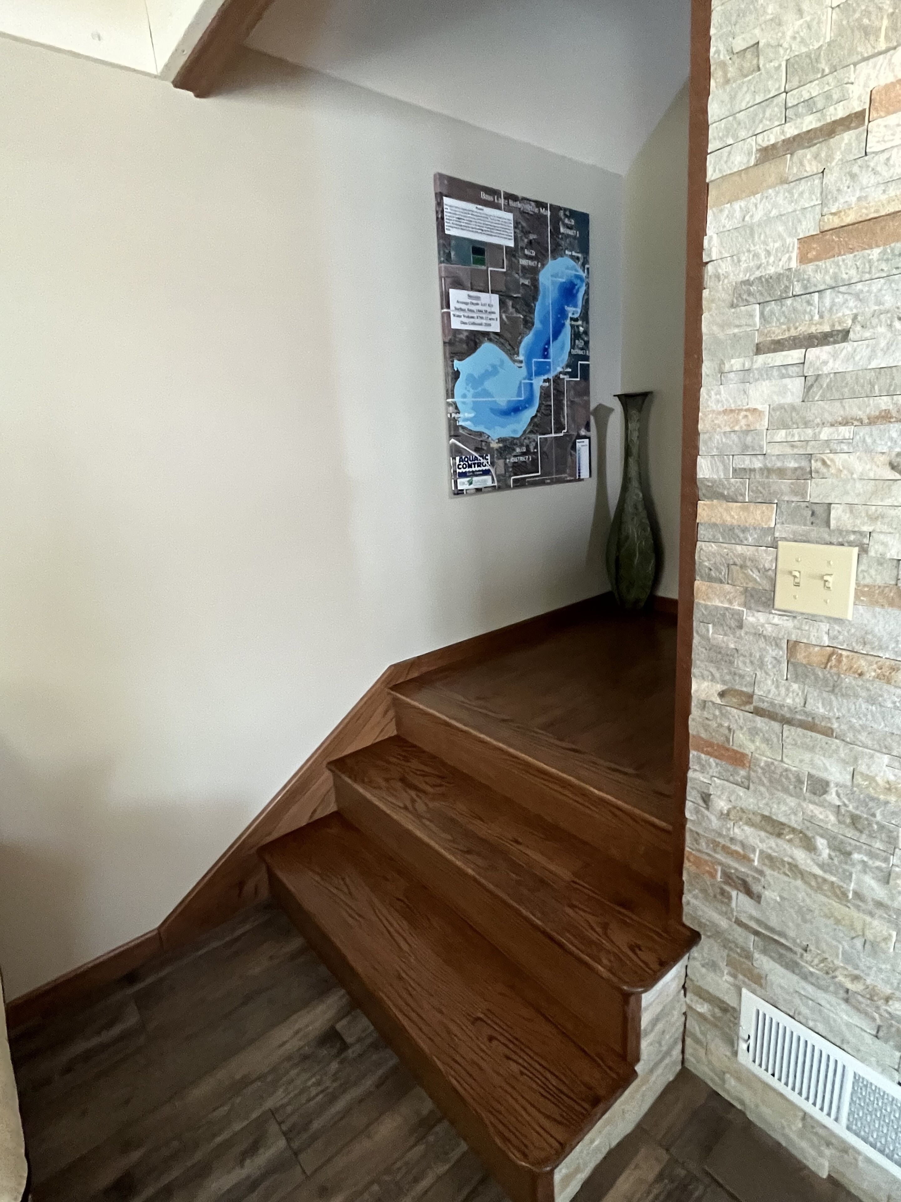 A staircase with wooden steps leading to a landing, a stone wall, and a map on the wall.