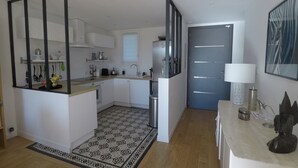 Moderni keittiö, jossa on valkoiset kaapit, pesuallas ja jääkaappi. Lattialla on kuvioitu matto ja ovessa on vaakasuorat linjat.