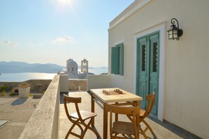 A terrace with a chessboard, wooden chairs, and a view of a church and sea.