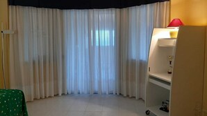 A room with a corner window, a green table, and a white cabinet with a red lamp. - Villa Rosanna (Patti)