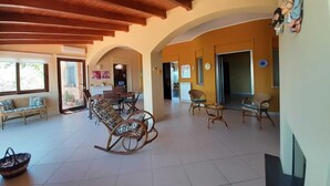 A spacious living area with a high wooden ceiling, a dining table with chairs, and a rocking chair. - Villa Rosanna (Patti)