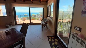 A spacious balcony with a view of the sea, a dining area with a table and chairs, and a large window. - Villa Rosanna (Patti)