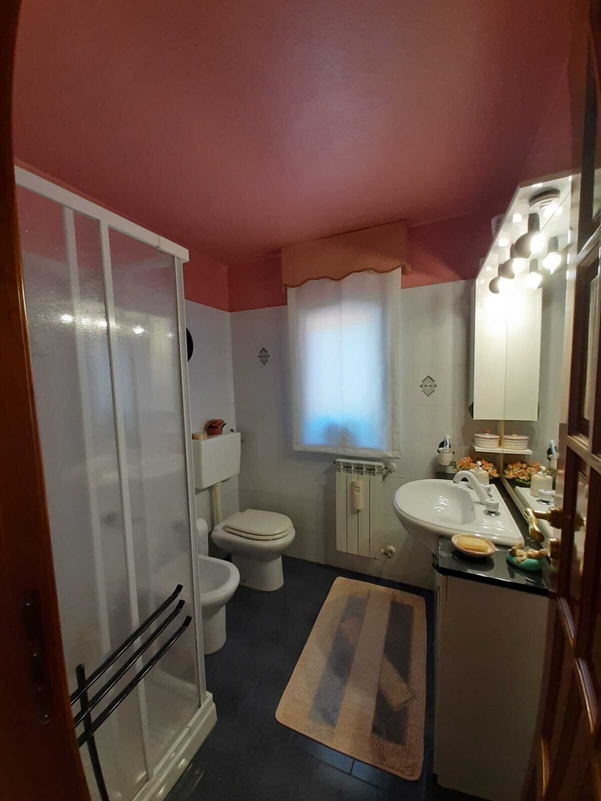 A bathroom with a shower, toilet, sink, and a small window with curtains.