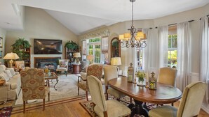 A spacious living room with a fireplace, comfortable seating, and a dining area with a chandelier. - Hamptons Summer Rental - secluded pool + 5 minutes to beach (East Quogue)