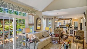 A spacious living room with a large window, a sofa, armchairs, and a coffee table. - Hamptons Summer Rental - secluded pool + 5 minutes to beach (East Quogue)
