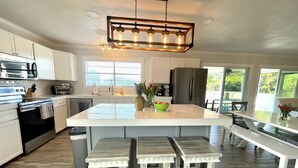Une cuisine moderne avec des meubles blancs, un îlot central doté de tabourets, un réfrigérateur en acier inoxydable et un luminaire suspendu.