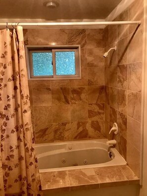 Een bad/douchecombinatie, een bubbelbad, een haardroger, handdoeken