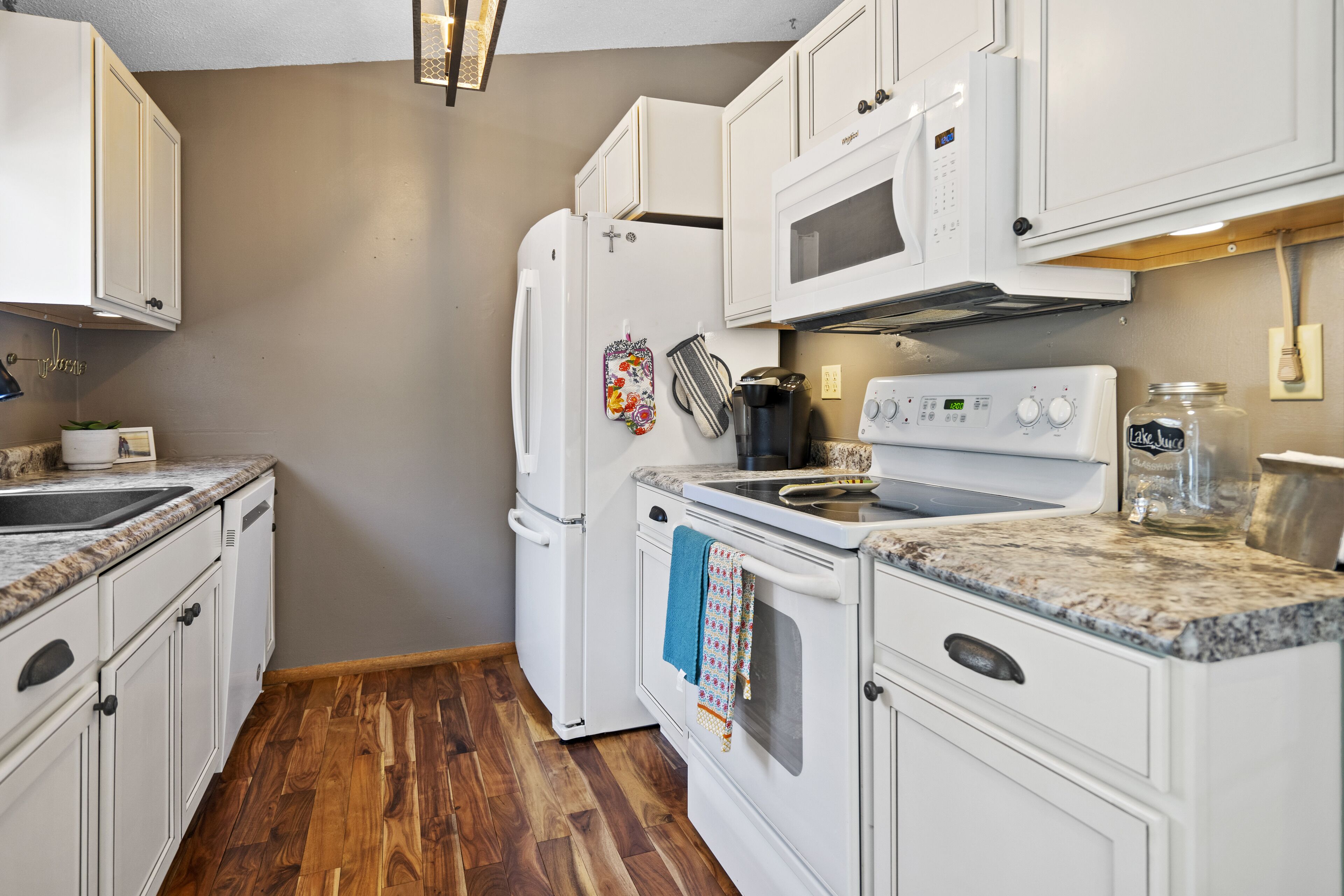 Una cocina con armarios blancos, microondas, estufa y refrigerador.