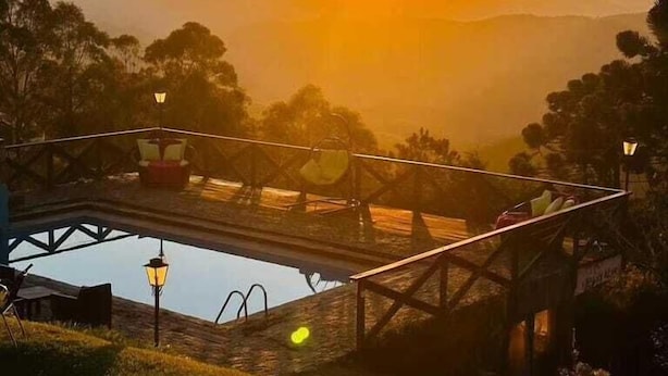 Vista do pôr do sol de uma ponte sobre um vale, com piscina e um gazebo.
