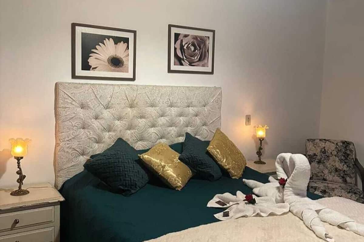 A bedroom with a tufted headboard, a green bedspread, and two framed floral pictures on the wall.