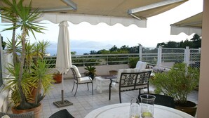 Una veranda coperta con mobili da esterno, piante in vaso e vista sul mare.