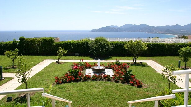 Un giardino con una fontana, un vialetto e vista mare e montagne.