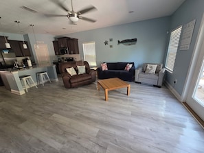 A spacious living area with a brown leather sofa, a wooden coffee table, and a kitchen in the background.