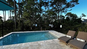 Ein Pool mit gefliestem Sonnendeck, umgeben von einem schwarzen Metallzaun und zwei Korbsstühlen.