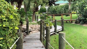 A wooden pathway leading to a grassy area with a wooden fence and a small bridge.