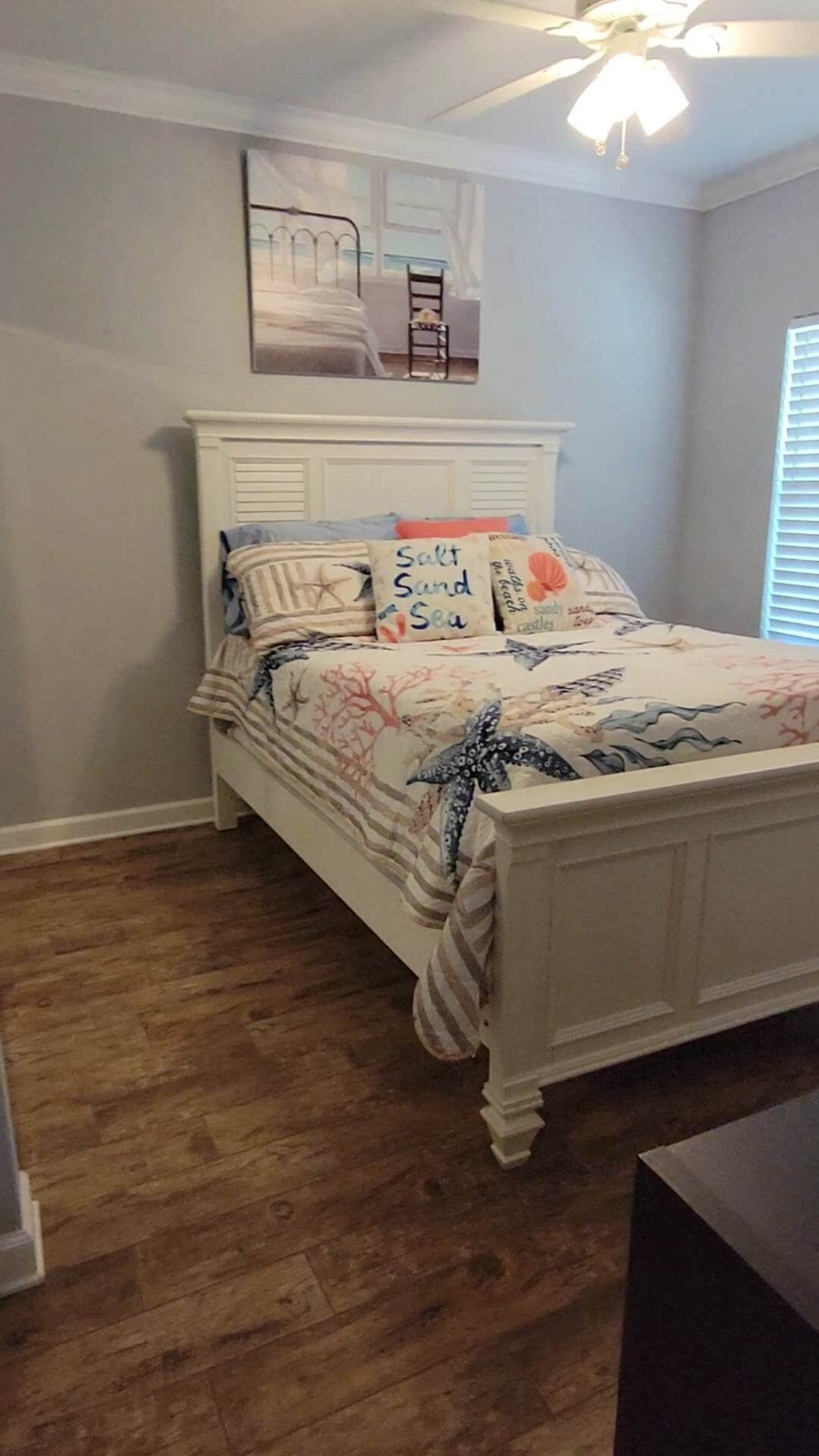 Un dormitorio con cama blanca, ropa de cama a rayas y un ventilador de techo.
