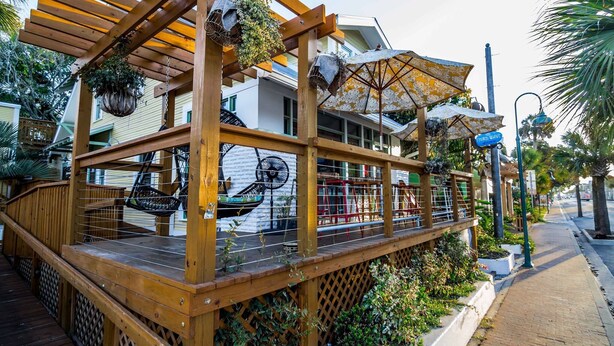 A wooden deck with hanging planters and umbrellas, a mural of a boat, and a sign reading "Third Wave."
