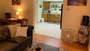 A living room with a leather sofa, a coffee table, a fan, and a kitchen visible through an open doorway. - #2 (Water) Home in the Heart of Utah- You are part of our community (Torrey)