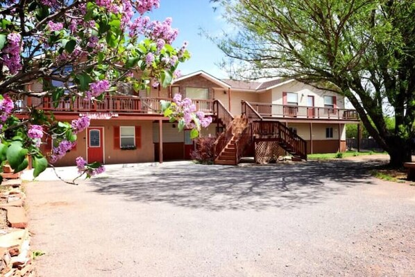 A two-story motel with a central staircase, a covered porch, and a tree with purple flowers.
