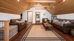 Ein gemütliches Loft mit Holzbalken, zwei Sofas, einem Couchtisch und einem großen Fenster.