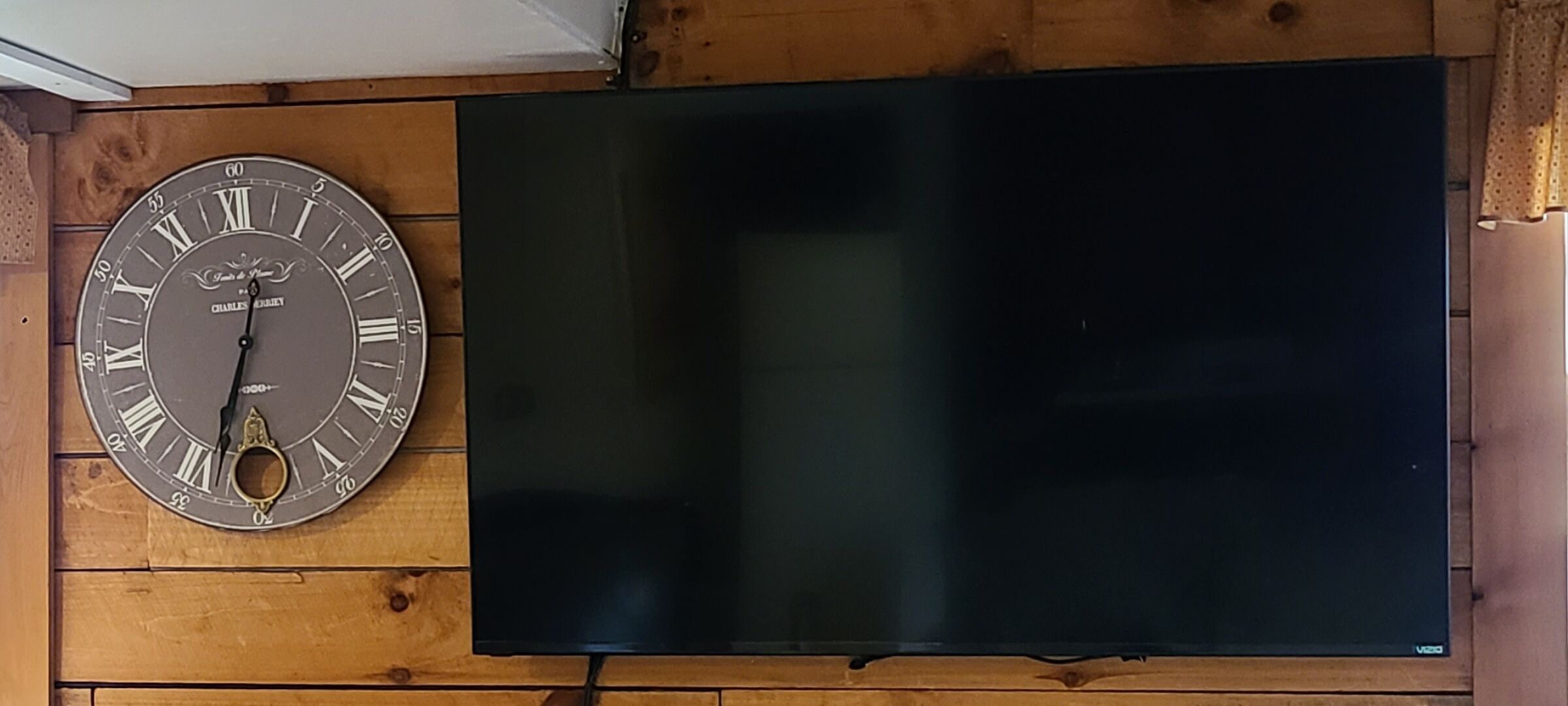 Seinälle kiinnitetty kello ja litteänäyttöinen televisio puisen seinän päällä.