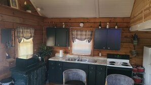 A compact kitchen with wooden walls, a central island with a sink, and a stove. - COZY CABIN AT PATOKA LAKE(in happy hollow) (Birdseye)