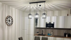 Een moderne keuken met een eethoek, met een klok, hanglampen en een inbouwoven.