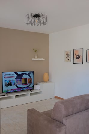 A living room with a flat-screen TV on a white stand, a beige sofa, a white console table with a vase and candle, and framed artwork on the wall. - La Meridiana App. 04 - The Perfect Spot for a Relaxing Vacation (Peschiera del Garda)