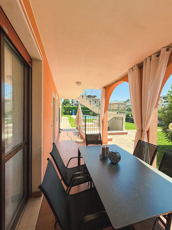 An outdoor patio area with a table and chairs, a view of a pool and buildings in the background.